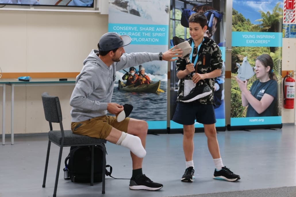 A young adult holds the artificial foot of a man who is sitting on a chair.