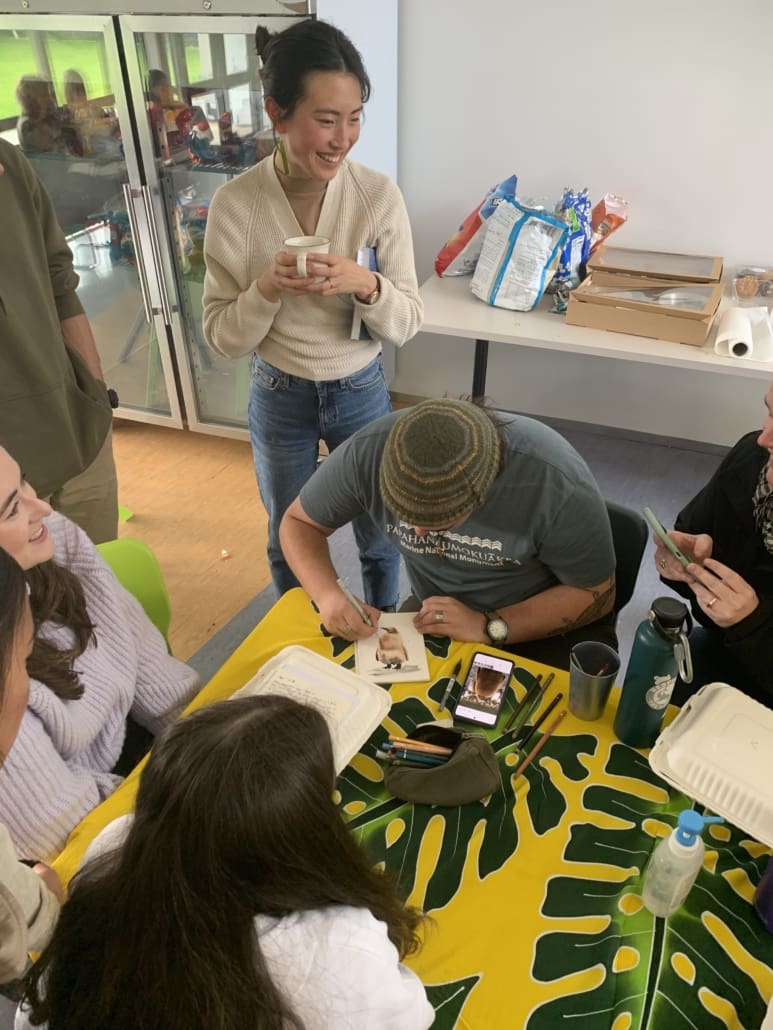 People watching someone paint a picture of a penguin.